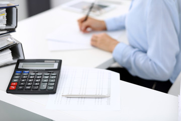 Calculator and binders with papers are waiting to be processed by business woman or bookkeeper back...