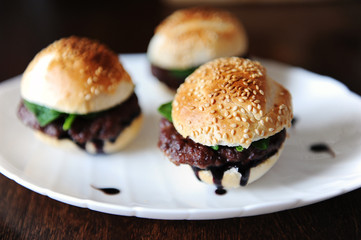 Three freshly cooked burgers on a white plate. Sesame bun, beef cutlet, spinach greens and flowing berry sauce.