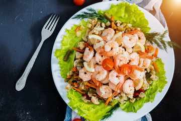 Flat lay of delicious shrimp with vegetables and greens on a black background, top view