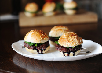 Three freshly cooked burgers on a white plate. Sesame bun, beef cutlet, spinach greens and flowing berry sauce.