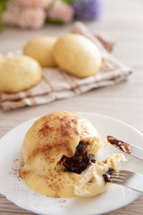 Germknödel oder Hefeklöße mit Pflaumenmusfüllung und Vanillesoße auf weißem Teller und hellem Holzuntergrund