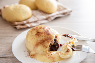 Germknödel oder Hefeklöße mit Pflaumenmusfüllung und Vanillesoße auf weißem Teller und hellem...