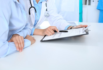Doctor and patient discussing something, just hands at the table, white background. Physician pointing into clipboard medication history form