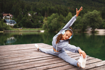 Young sports woman stretching legs at dock on the lake in the mountains