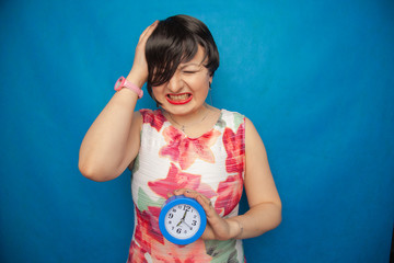 angry screaming unhappy girl holding a round alarm clock on blue studio background