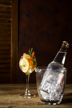Bottle and a glass of alcohol with ice and orange on a dark wooden background