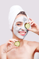 Young woman with cosmetics on face applying cucumber to her eye