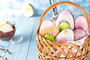 Colorful easter eggs and glazed cookies in basket on blue wooden background