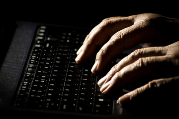 Danger concept on the internet, the hands of an elderly man on a laptop keyboard