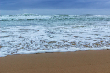 Fototapeta na wymiar close up of sand and waves with sea foam