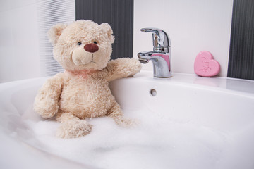 A cute teddy bear is sitting in the basin and washing. 
