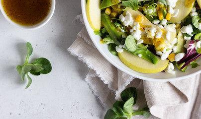 Mix salad with corn, apple, avocado and fresh farm cottage cheese. Healthy and diet food concept. Light concrete background. Copy space.