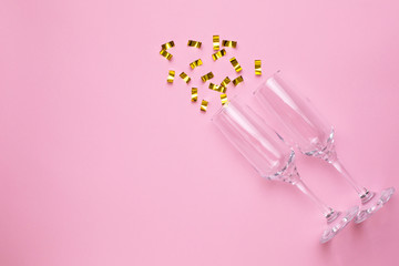 Obraz na płótnie Canvas Champagne glasses with golden confetti on pink color paper background minimal style