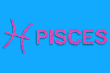 Symbol of astrological sign and word pisces cut out of purple paper on blue table. Top view. Horoscope concept