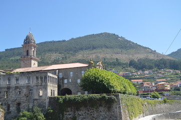 Fototapeta na wymiar Side Facade Of The Monastery Of Santa Maria Of The Oia With Views Over The Village Of Oya. Nature, Architecture, History, Travel. August 16, 2014. Oya, Pontevedra, Galicia, Spain.