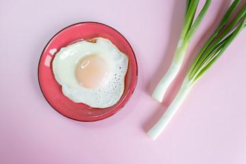 Sunny side up egg. Fried eggs with green onions on a pink background