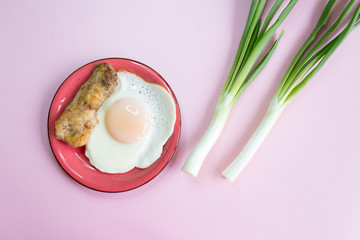 plate of hot egg, bacon and green onions, isolated on pink background, top view