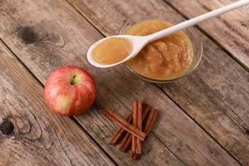 fresh homemade apple jam, apple puree with cinnamon in a bowl with wooden spoon and apples on wooden rustic table