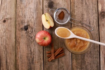 fresh homemade apple jam, apple puree with cinnamon in a bowl with wooden spoon and apples on wooden rustic table