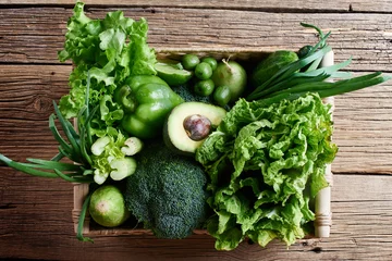 Tuinposter Green vegetables and fruits and greens in a brown wicker basket on a wooden background. Healthy eating concept © amixstudio