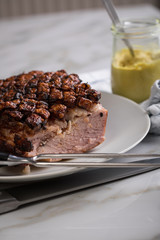 Deutscher Krustenbraten aus Schweinefleisch mit Senf auf Teller mit Küchenmesser und Fleischgabel auf Marmor Hintergrund