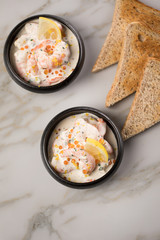 Garnelen Salat mit Lachs Kaviar,  Kräuter, Zitrone, und Vollkorn Toast Brot in schwarzer Schale auf Marmor Hintergrund