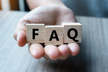 Business man hand holding wooden cube with FAQ text ( frequently asked questions) on table...