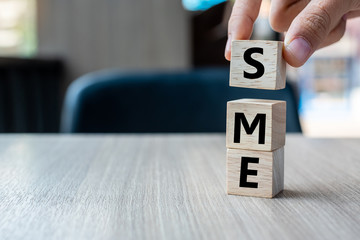 Business man hand holding wooden cube with SME text (Small Medium Enterprise) on table background....