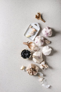 Variety of fresh organic garlic bulbs whole and peeled and cloves of black fermented garlic with ceramic grater over grey spotted background. Flat lay, space