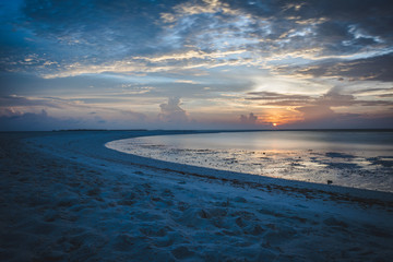 Sunset in the Maldives with reflection of the Sun in the water and blue and orange colored clouds in the sky