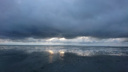 Sonnenuntergang hinter Wolkenwand spiegelt sich im Wattenmeer bei Ebbe