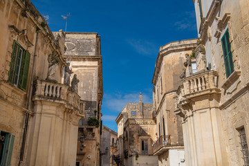 Fototapeta na wymiar Lecce, Puglia, Italy - Medieval street and historical center in the old town. View and detail of an ancient gate or door, statues and facade of houses. A region of Apulia