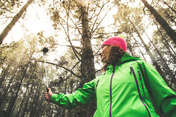 View from below middle aged woman brown curly hair in mountain forest takes selfie with camera...