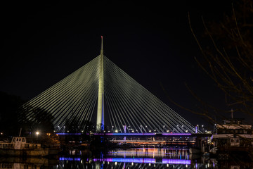 night picture of the bridge on the ada with reflection in the clear water while the lighting is overflowing