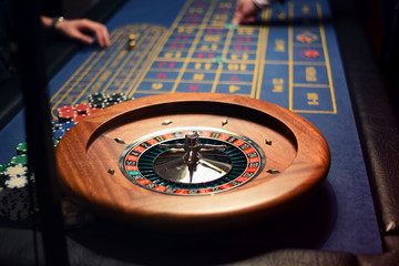 Roullette players in casino. Close up of roulette wheel and chips in the background.