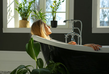 side view of beautiful relaxed woman lying in luxurious bathtub, closed eyes, lots of light, green...