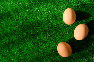 Top view of Easter decoration from three eggs, lying on grass as a green background with copy space.