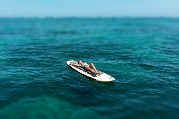 Naklejka premium A beautiful young woman relaxes on a SUP board in the sea near the island. Drone shot