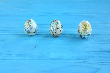 Beautiful three quail Easter eggs with blue sparkle shiny decor and selective focus on blue wooden textured table. Traditional Easter symbol on rustic background. Spring Easter card 