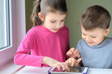 White caucasian toddler boy and beautiful girl playing together on tablet games. Portrait of a happiness little brother and sister. Children play a computer game on the tablet