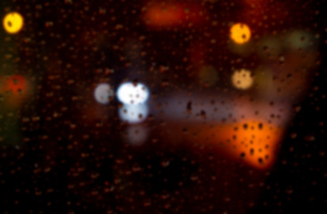 Blurred bokeh night town background with light blinking colored stars and raindrops on glass city ​​view