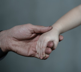 Closeup senior man and baby girl holding hands together on dark background