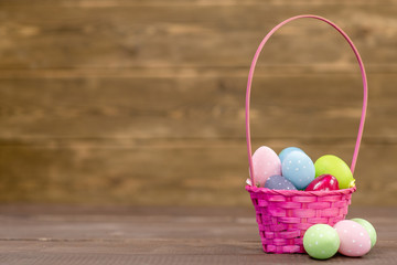 Easter basket filled with colorful eggs on wooden background. Empty space foe text