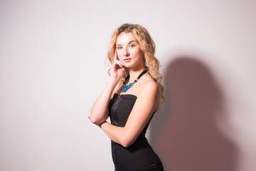 Fototapeta premium Sexy blond elegant woman in black dress standing on white background with copy space