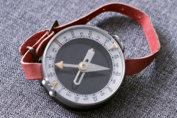 Old wrist compass with red strap lying on fabric
