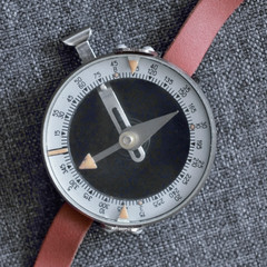Old wrist compass with red strap lying on fabric
