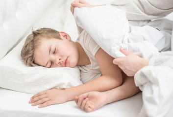 Obraz na płótnie Canvas Mother covering little sleeping boy with blanket