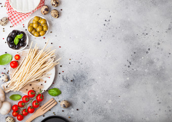 Homemade spaghetti pasta with quail eggs with bottle of tomato sauce and cheese on kitchen background. Classic italian village food. Garlic, champignons, black and green olives, pan and spatula.