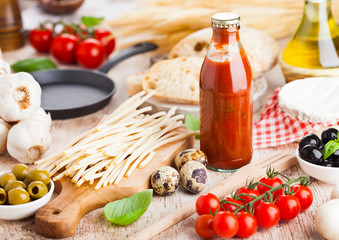 Homemade spaghetti pasta with quail eggs with bottle of tomato sauce and cheese on wooden background. Classic italian village food. Garlic, black and green olives, oil and bread. Frying pan