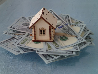 A stack of dollars and a toy wooden house